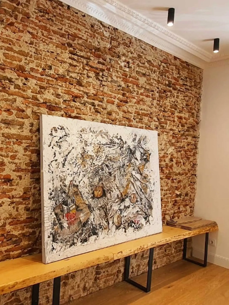 Cuadro abstracto apoyado sobre repisa de madera y pared de ladrillo en bruto