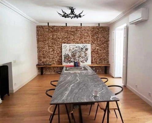 Despacho de reuniones de diseño de empresa de reformas e interiorismo en Madrid con gran mesa rectagulay y pared de ladrillo en bruto con un cuadro abstracto