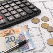 coste-reforma-piso-60-metros Calculadora, planos de vivienda, monedas y billetes de euro sobre una mesa de trabajo para representar el precio de reforma en Madrid de piso de 60 metros cuadrados.