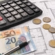 Calculadora, planos de vivienda, monedas y billetes de euro sobre una mesa de trabajo para representar el precio de reforma en Madrid de piso de 60 metros cuadrados.