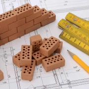Mini ladrillos construyendo una pared, un bolígrafo y unas reglas sobre una planos de la reforma integral de una vivienda