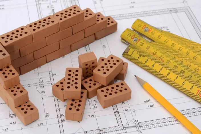 Mini ladrillos construyendo una pared, un bolígrafo y unas reglas sobre una planos de la reforma integral de una vivienda