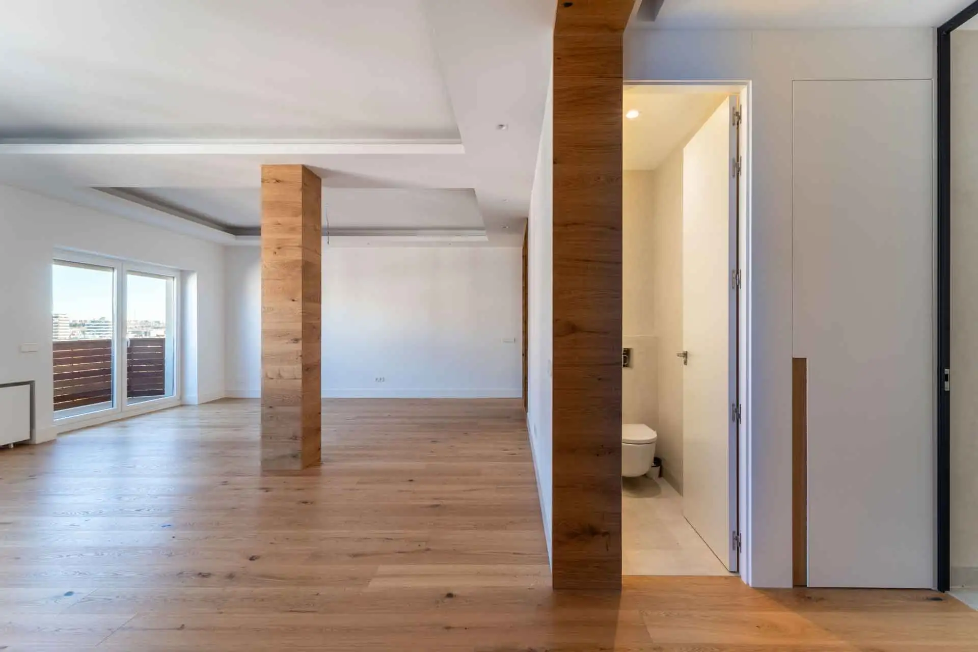 amplio salón con viga forrada en madera y cuarto de baño con puerta abierta