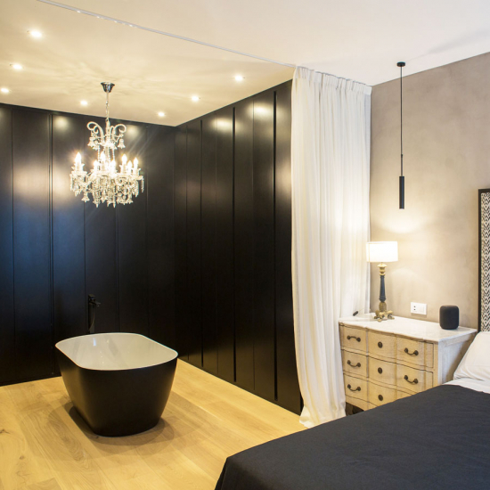 Bañera independiente de color negro mate y el interior en color blanco en la zona de armarios con puertas en negro en dormitorio con cama de matrimonio de vivienda en Madrid