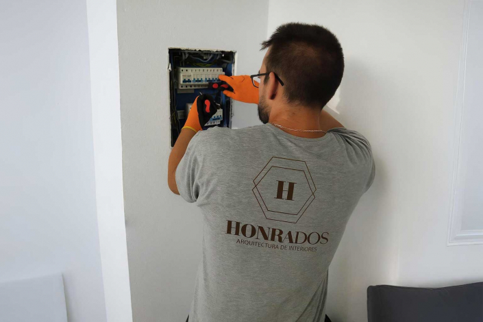 Un electricista de la empresa de reformas en Madrid Honrados, con guantes de seguridad, trabaja en el cuadro de luces para cambiar la instalación eléctrica de una vivienda.