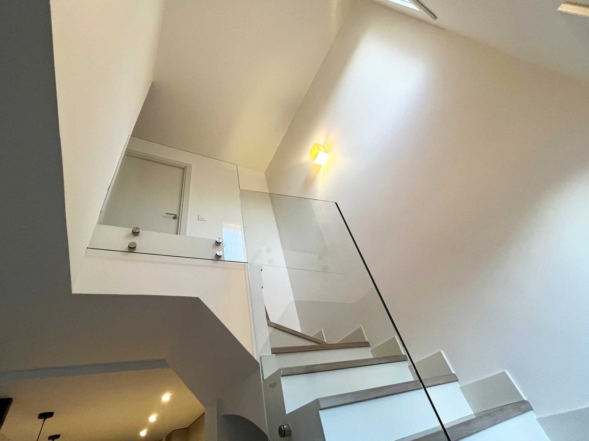 Escalera con barandilla de vidrio invisible de chalet hacia la zona de dormitorios hecha por la empresa de reformas en Pozuelo Honrados