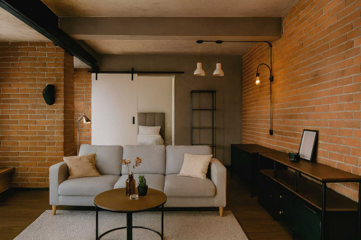 interior de una vivienda que anteriormente fue un local comercial en Madrid. Decorada con un estilo industrial, la imagen destaca las paredes de ladrillo visto, elementos metálicos y una decoración que refleja su pasado comercial pero adaptada a su nuevo uso residencial