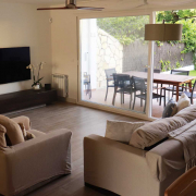 Amplio y luminoso salón-comedor resultado de una reforma de chalet en Pozuelo de Alarcón. Se aprecian grandes cristaleras correderas que conectan el interior con el jardín, sofás de tonos neutros, y un suelo de tarima que aporta calidez al espacio