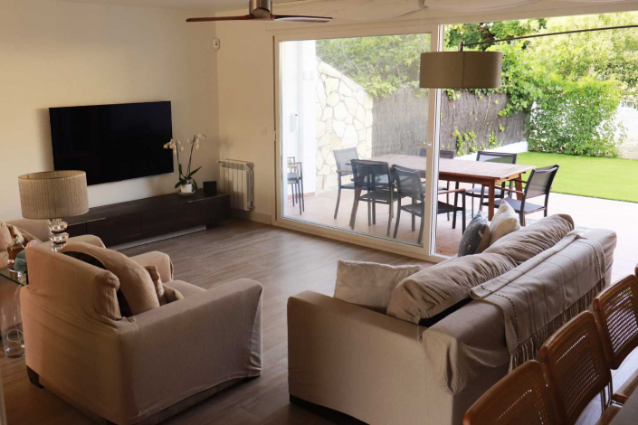 Amplio y luminoso salón-comedor resultado de una reforma de chalet en Pozuelo de Alarcón. Se aprecian grandes cristaleras correderas que conectan el interior con el jardín, sofás de tonos neutros, y un suelo de tarima que aporta calidez al espacio