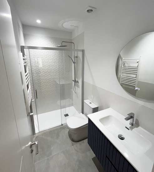 Baño moderno con azulejo geométrico y mueble azul oscuro en la reforma en Tirso de Molina.