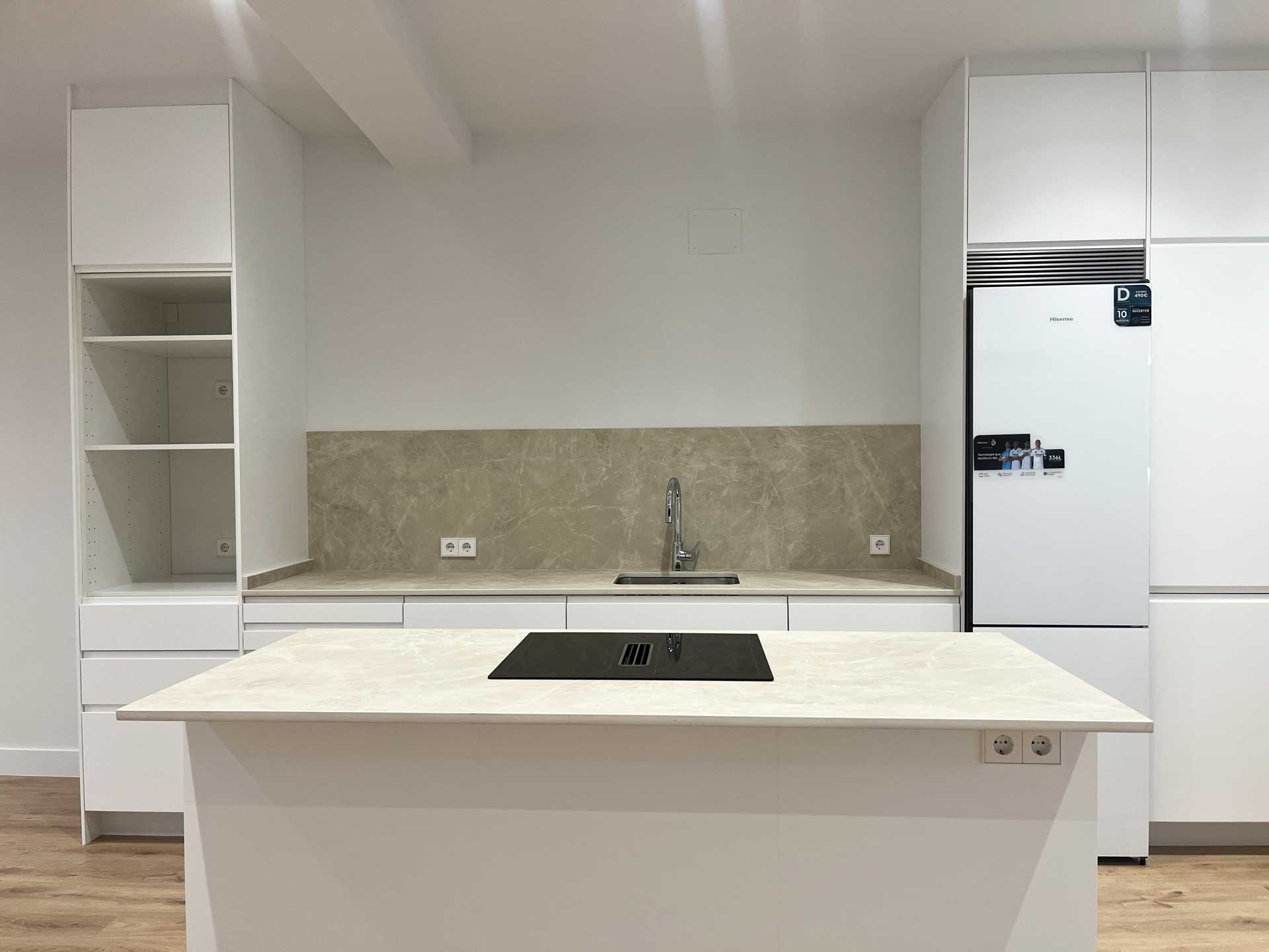 Detalle de la isla de cocina con placa de inducción, encimera y salpicadero de mármol después de la reforma integral en vivienda en Tirso de Molina