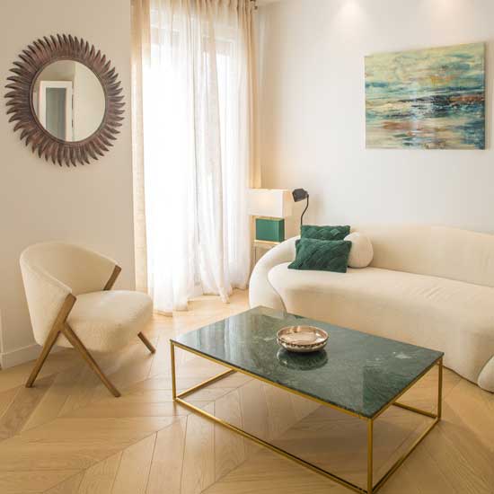 Salón con sofá con líneas curvas color crema, mesa de centro de mármol verde y espejo sol, reflejando tendencias de decoración para 2026