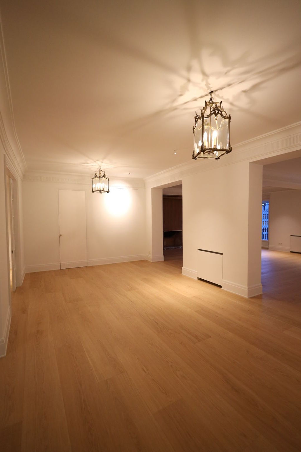 Amplia y luminosa entrada tras una reforma integral en Marqués de Salamanca, con suelo de madera natural, paredes blancas, molduras clásicas, espacios abiertos y lámparas decorativas que combinan elegancia clásica y diseño contemporáneo.