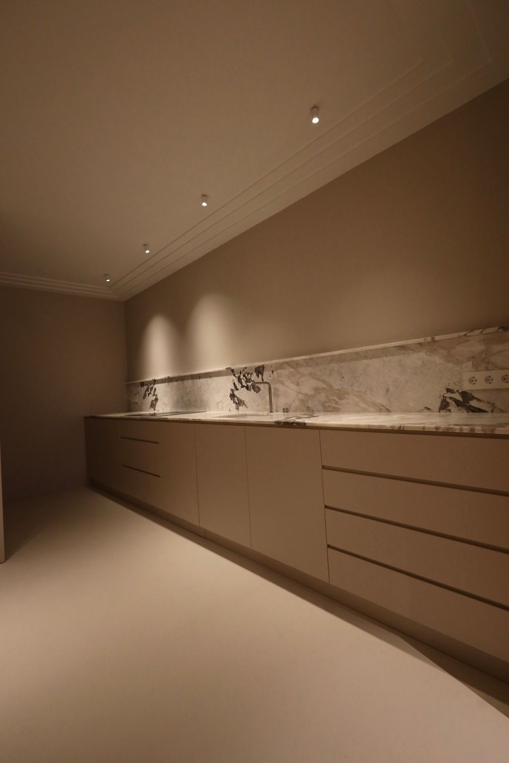 Cocina de diseño contemporáneo tras una reforma integral en Marqués de Salamanca, con mobiliario a medida en tonos neutros, encimera y frontal de mármol, iluminación empotrada y distribución lineal que aporta elegancia, funcionalidad y amplitud.