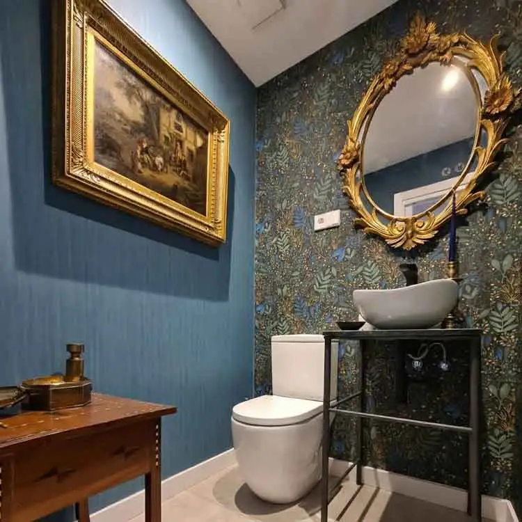 Baño en urbanización La finca con paredes con papel pintado Baño de vivienda en urbanización La finca de La Moraleja con paredes con papel pintado de estilo botánico, lavabo sobre encimera y espejo dorado clásico decorativo.