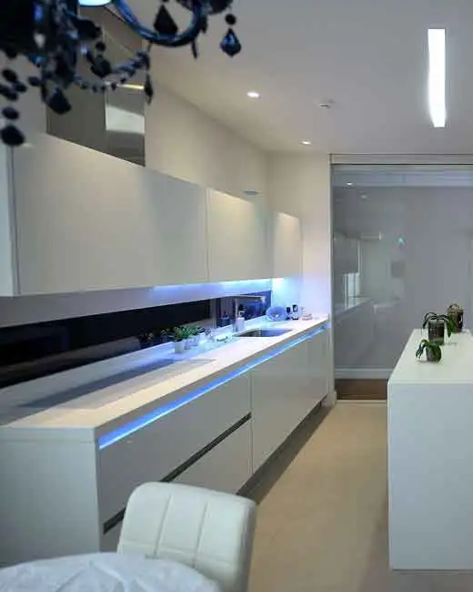 Cocina con zona de trabajo iluminada con luces LED | 5 errores a evitar al diseñar la cocina. Cocina con luces LED que iluminan el espacio de trabajo, muebles blancos de líneas modernas e isla central, como ejemplo para explicar los cinco errores que debes evitar al diseñar la cocina.