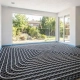 Instalación de suelo radiante en una vivienda unifamiliar durante una reforma integral en Madrid. Se aprecia la colocación de los tubos sobre una base aislante negra para un sistema de calefacción de alta eficiencia energética, preparado para funcionar con una instalación de aerotermia. La estancia cuenta con grandes ventanales que aportan abundante luz natural y vistas al jardín exterior. Esta actuación puede formar parte de proyectos de rehabilitación energética susceptibles de acogerse a una subvención dentro del Plan Rehabilita 2026 de Madrid, mejorando el confort térmico y reduciendo el consumo energético de la vivienda.