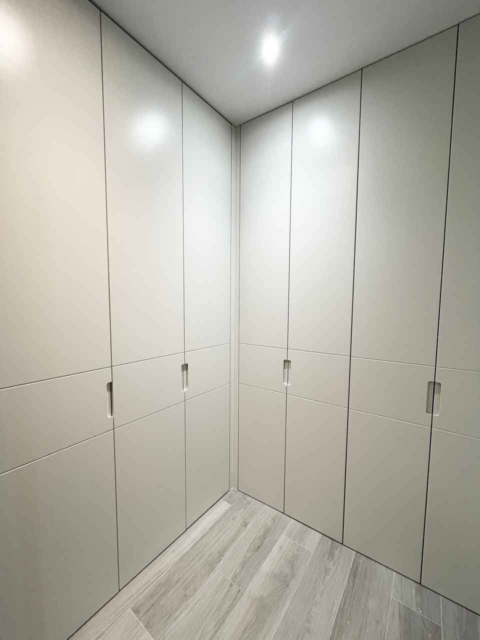 oficina-ciudad-barcelona-madrid-convertida-dos-viviendas-armarios-pasillo-piso-uno Imagen de la carpintería interior del Piso Uno. Se muestran armarios empotrados de suelo a techo con tiradores uñeros, instalados profesionalmente para maximizar el espacio de almacenamiento en el proyecto de oficina en Pacífico convertida en dos viviendas. Suelo de tarima gris a juego.