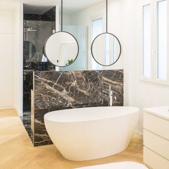 Dormitorio Moncloa muro revestido porcelánico gran formato Dormitorio con baño en suite, tipo hotel en Moncloa-Madrid, con bañera, independiente, en color blanco, con pared a media altura, revestida con porcelánico de gran formato, efecto mármol oscuro.