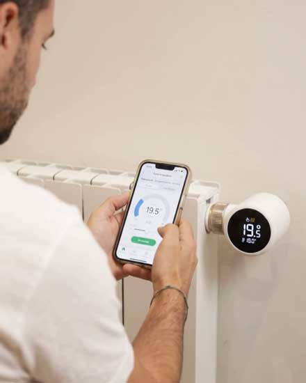 Persona ajustando la temperatura de un radiador con un cabezal inteligente con termostato digital desde el móvil.